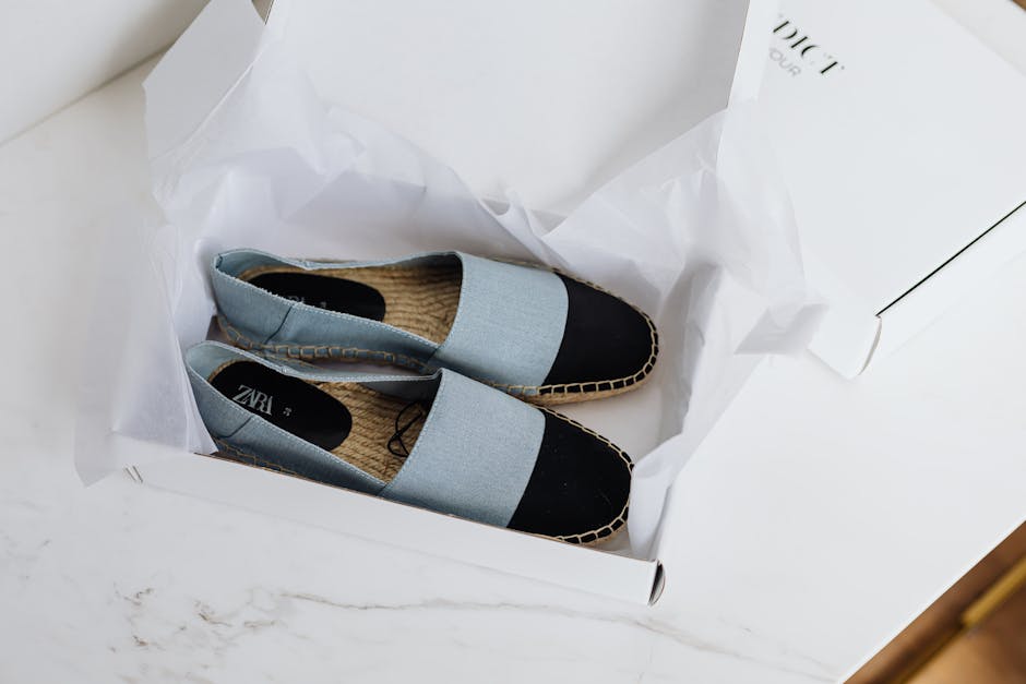 Pair of casual flat slip-on shoes with black toe caps and light blue straps in a white box